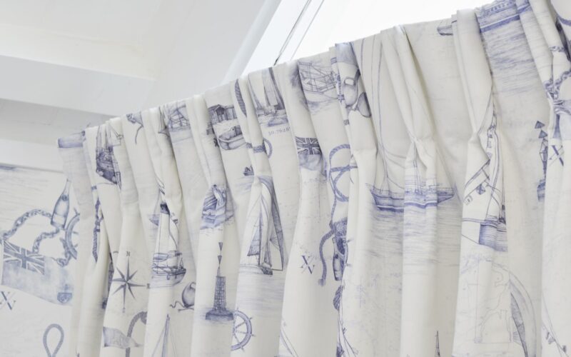 The curtains are white with a blue nautical pattern featuring boats, ships, and anchors. The rod is white and appears to be curved.