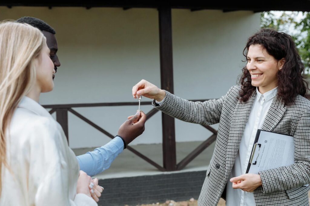Real estate agent giving house keys to a happy couple outside their new home.