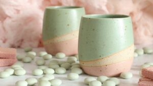Two pastel-coloured ceramic tumblers, a light mint green on top and a soft pink on the bottom, with a creamy beige stripe separating the two colours.
