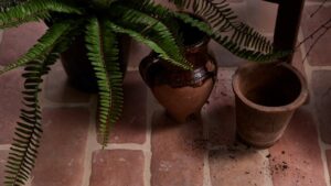 The image shows a close-up, overhead view of a rustic-looking floor made of reddish-brown terracotta tiles, laid in a brick-like pattern.