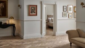 A stylish room featuring Woodpecker Flooring's Orkney Pewter Oak Herringbone Engineered Wood Flooring. The flooring is laid in a classic herringbone pattern, with varying shades of light brown and grey tones. The walls are painted in a light, neutral colour with white wainscoting and moulding.